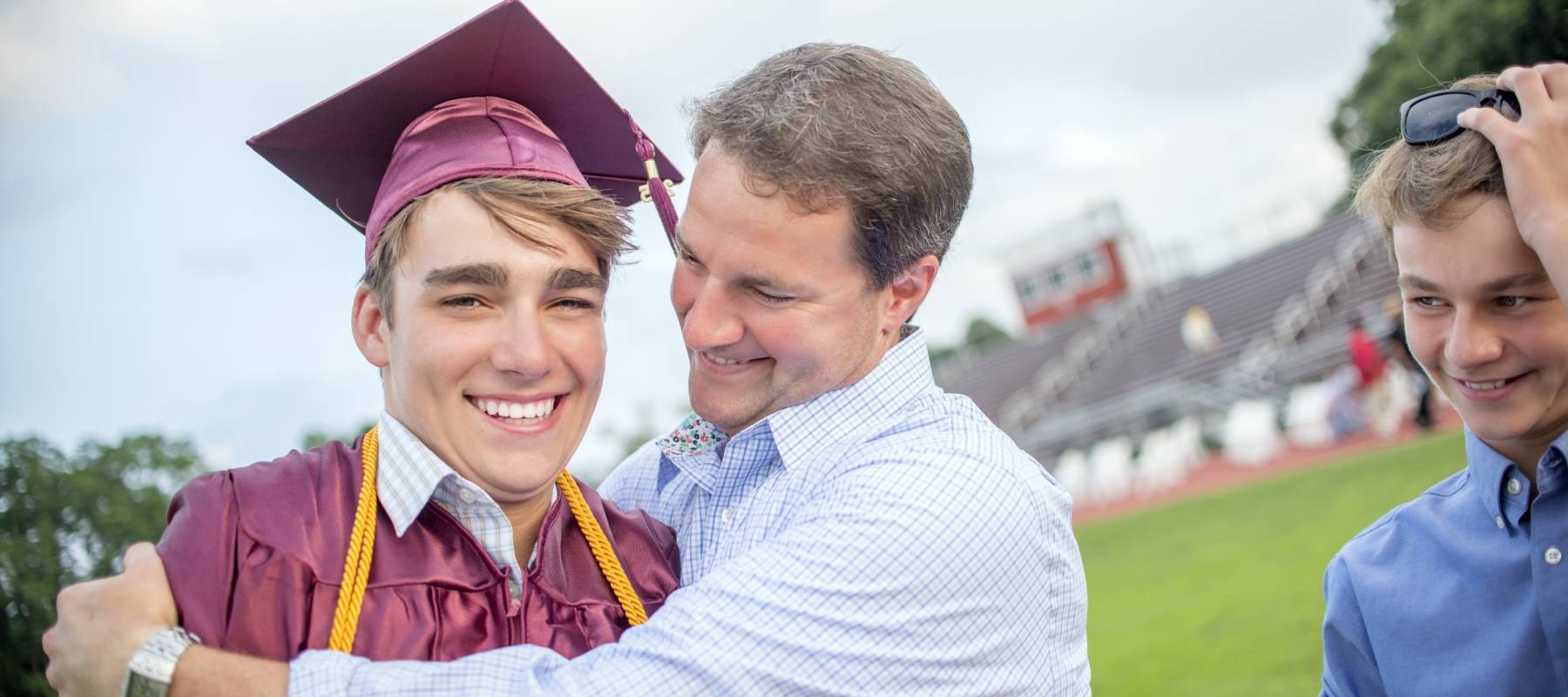 Young man being hugged by father at graduation ceremony