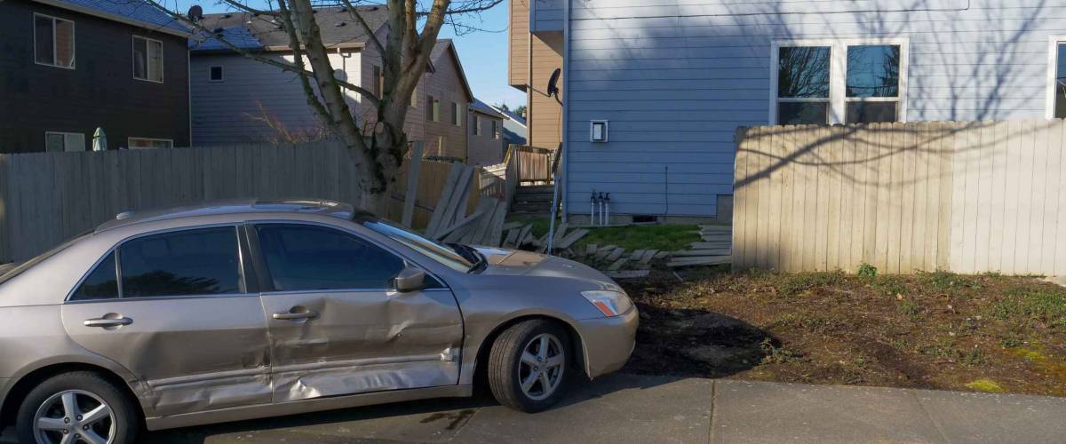 Car crash scene after auto has plowed into a fence next to a house.