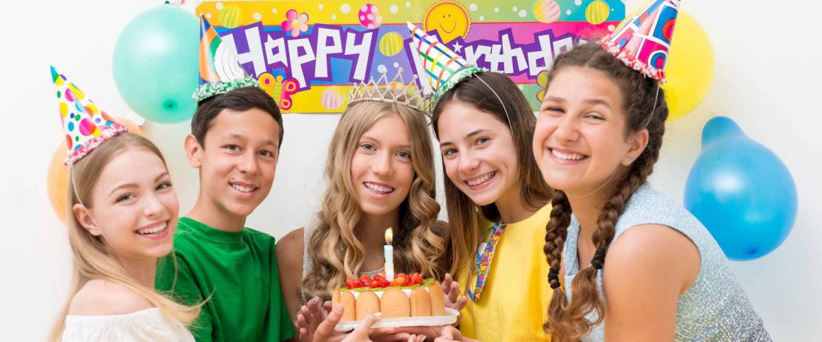A group of teenagers at a birthday party holding the cake