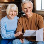Happy relationships. Joyful positive elderly couple sitting together and smiling while checking the bills