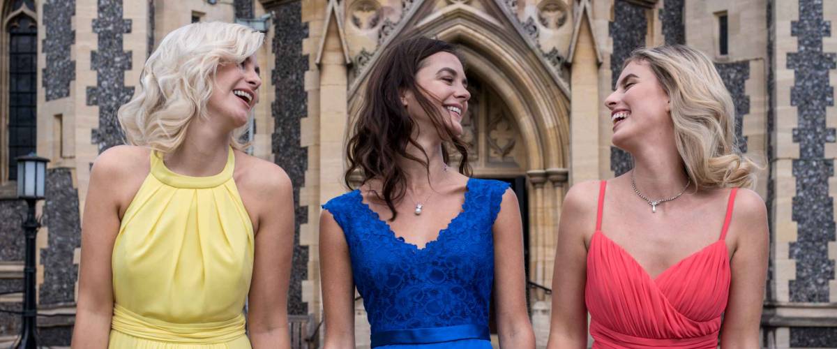 Three beautiful european bridesmaids in red, yellow and blue dresses posing outside a church