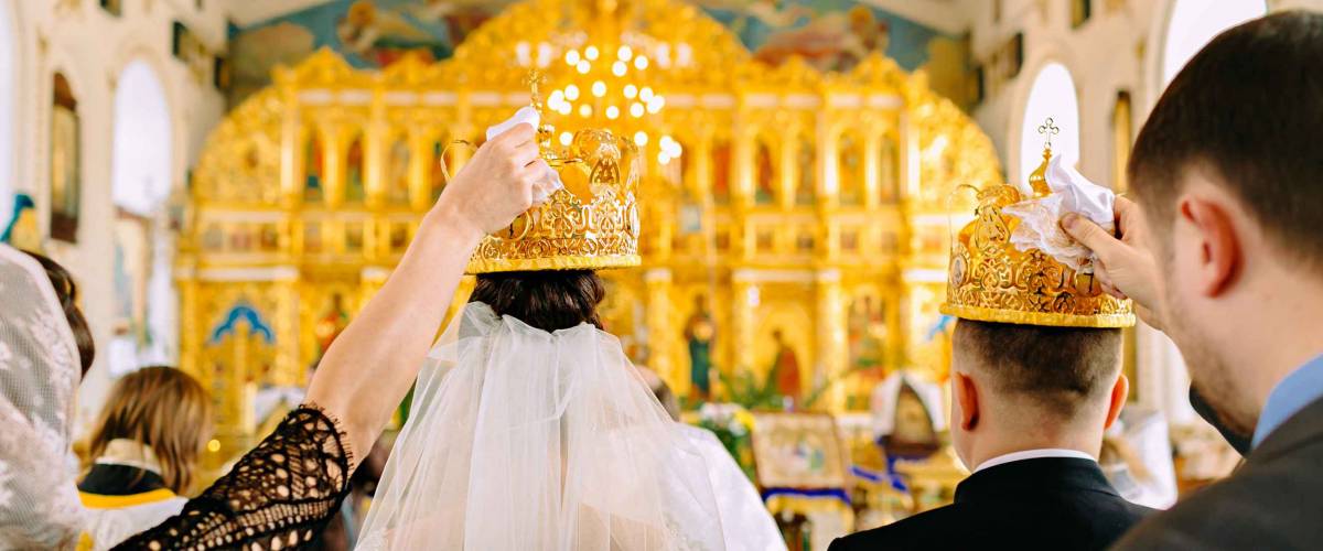 The witnesses of the newlyweds hold the golden crowns in the church over the heads of the bride and groom. Back view