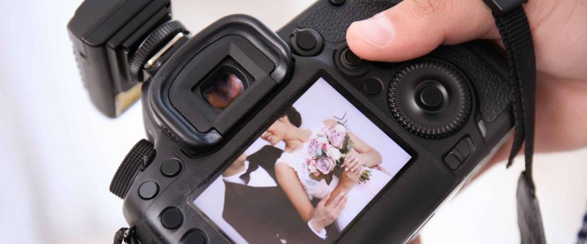 Professional photographer holding camera with lovely wedding couple on display