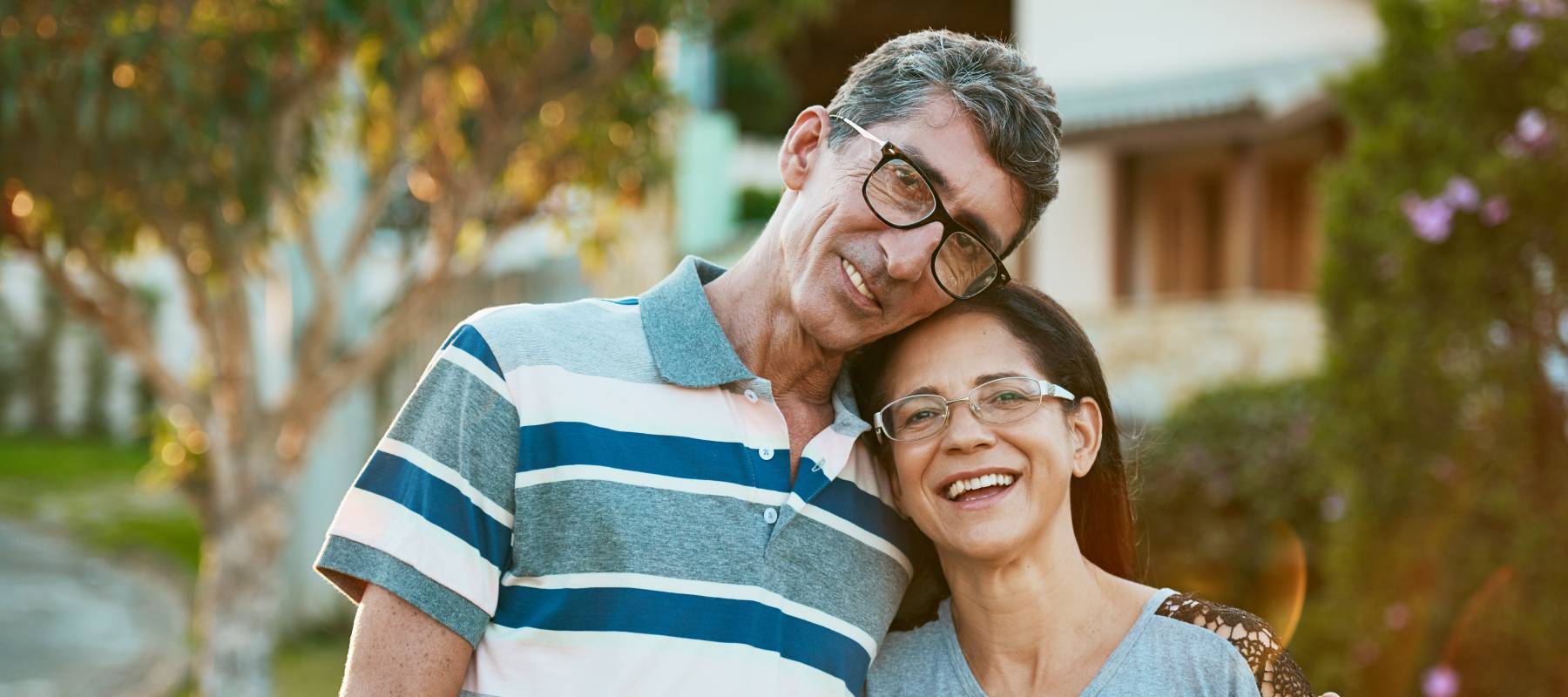 Caucasian couple on their mid-50s smiling in front of their home