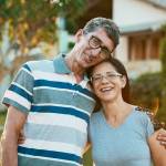 Caucasian couple on their mid-50s smiling in front of their home