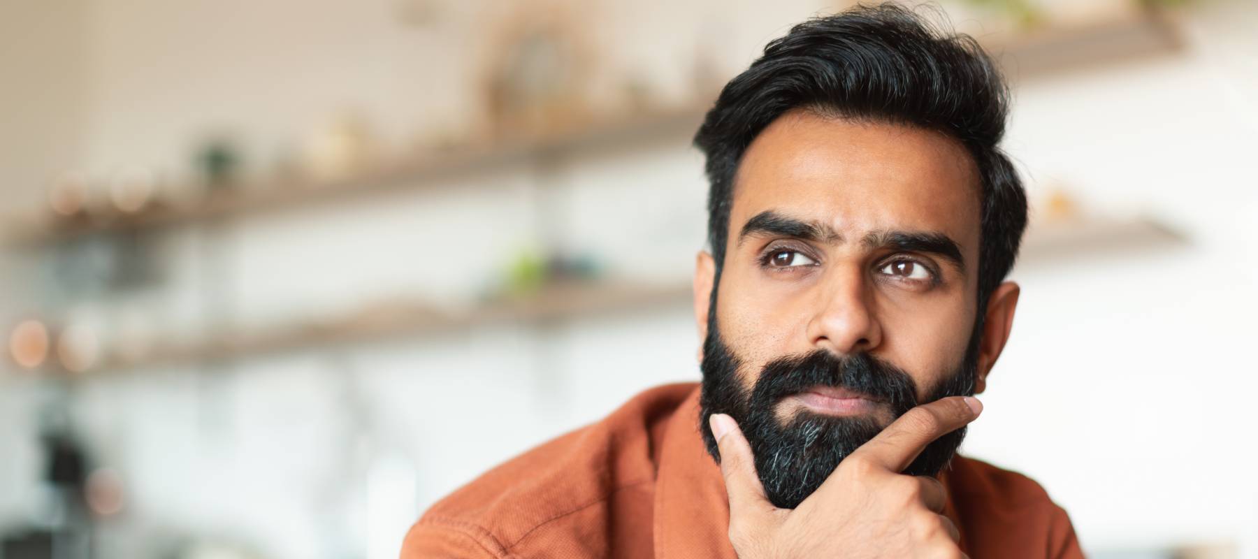 Portrait of pensive young man thinking in living room.
