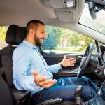 Side view of happy and surprised young businessman driving car.
