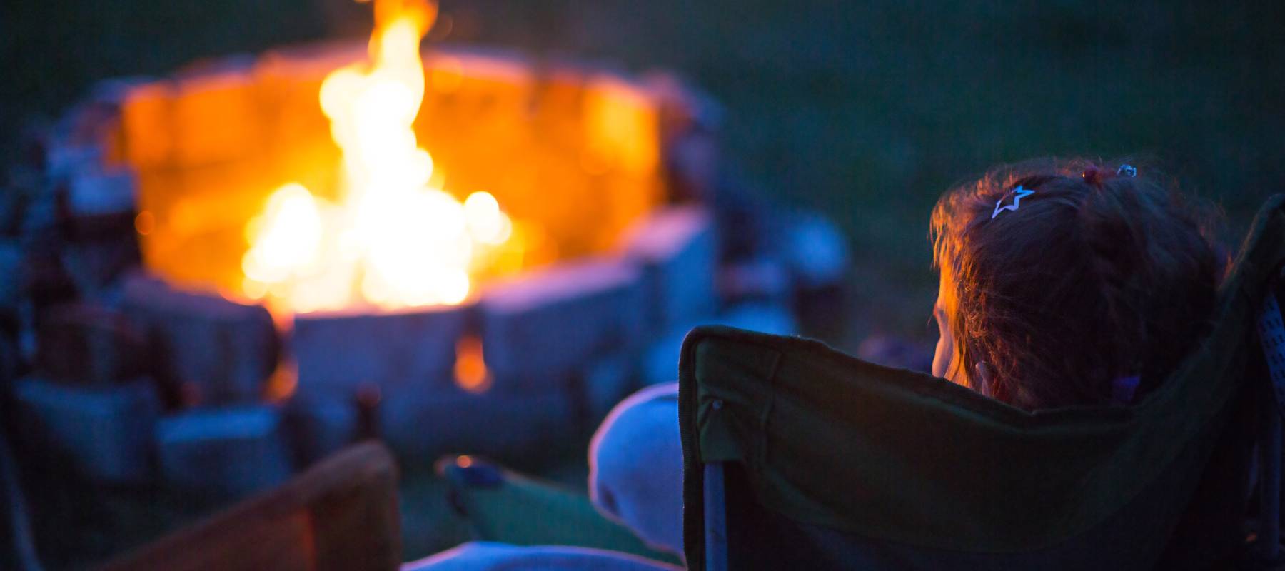Dad and daughter sit at night by the fire.