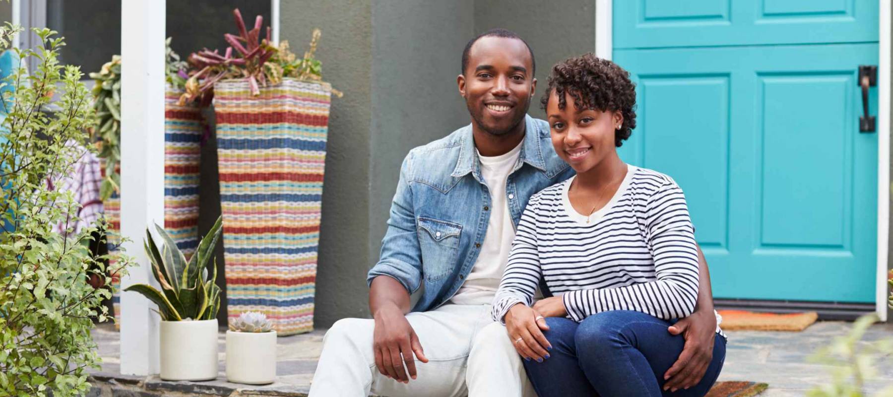Young couple sit looking to camera outside their new house