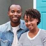 Young couple sit looking to camera outside their new house