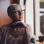 Senior woman sitting at a table, looking out a window.