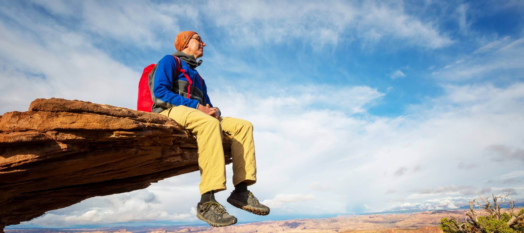 Senior man sitting on edge of rock cliff.