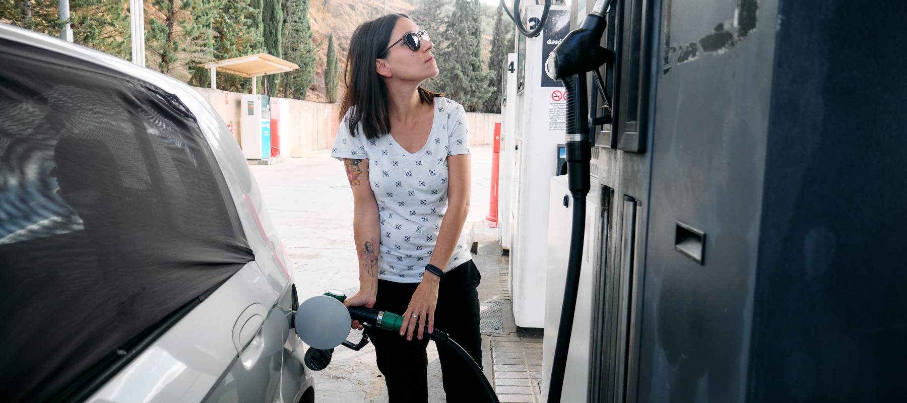 a young brunette woman filling up with gasoline herself at a small gas station
