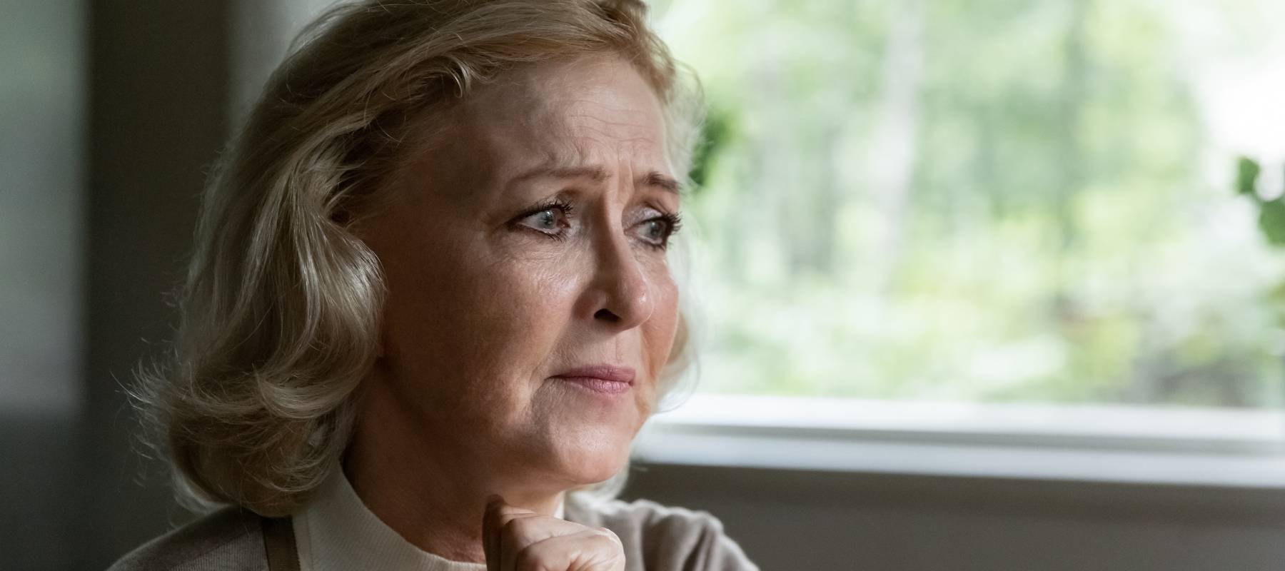 An older woman ponders by a window.