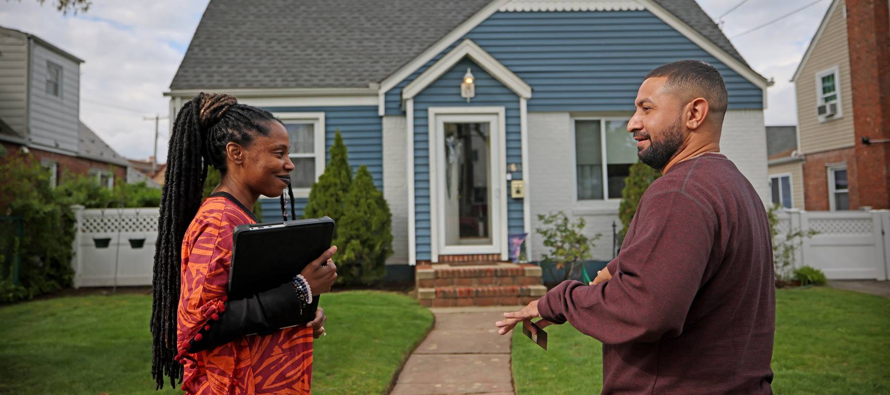 Real estate broker speaks with a potential buyer outside a house.