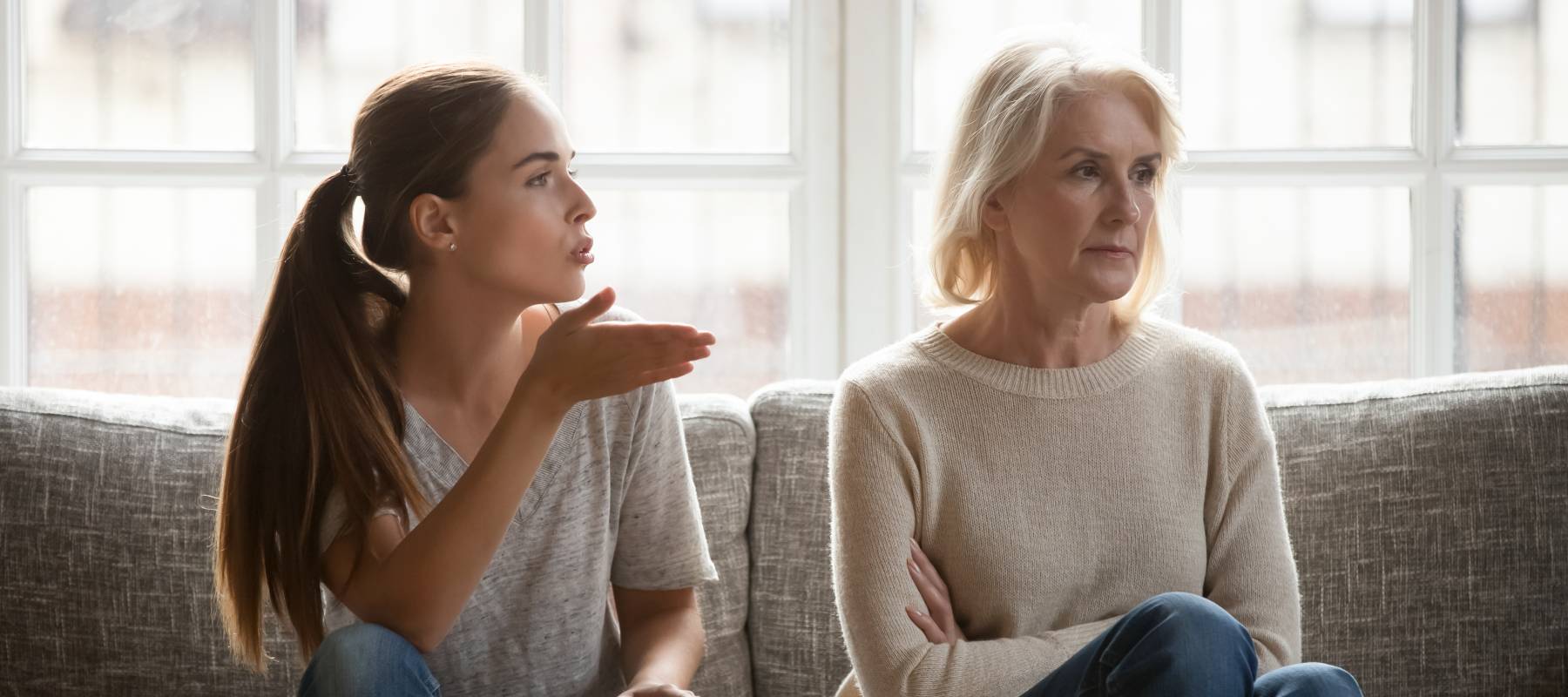 Annoyed daughter expressing frustration to mother on couch.