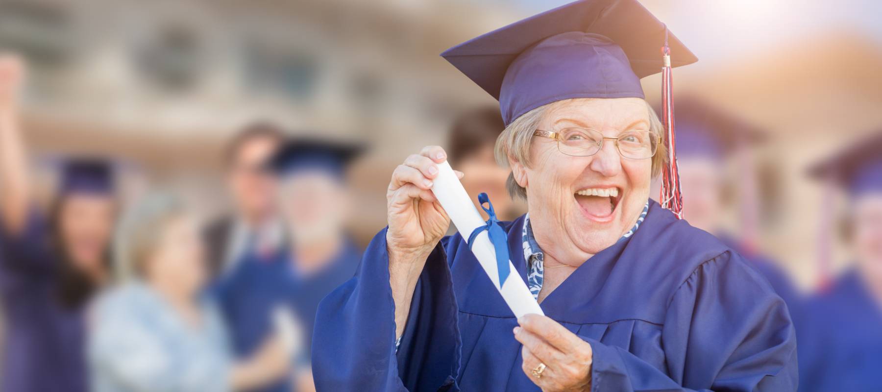 A happy older female in grad cap and gown, holding a rolled diploma.