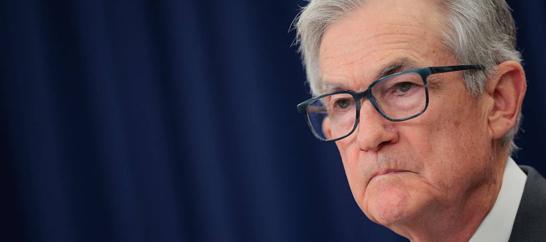 Federal Reserve chair Jerome Powell stares grimly at the camera with his mouth in a distinctive frown.