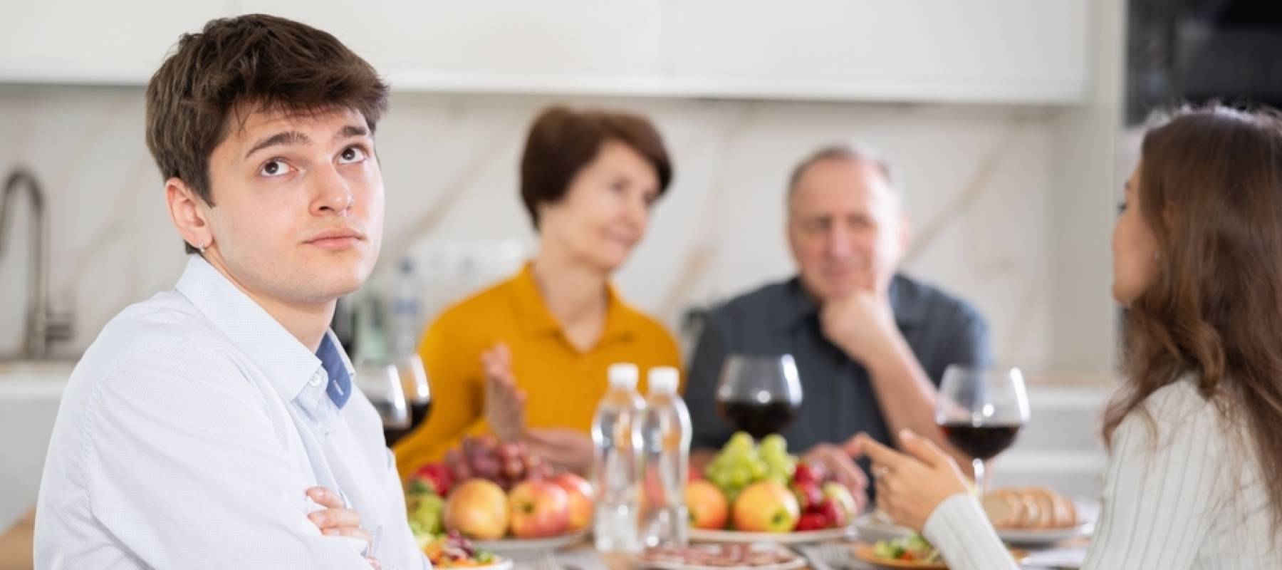 A young man looks away from his family at the dinner table.