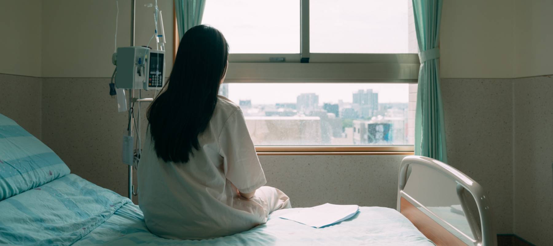 back view of lonely young asian woman sitting on bed in hospital ward