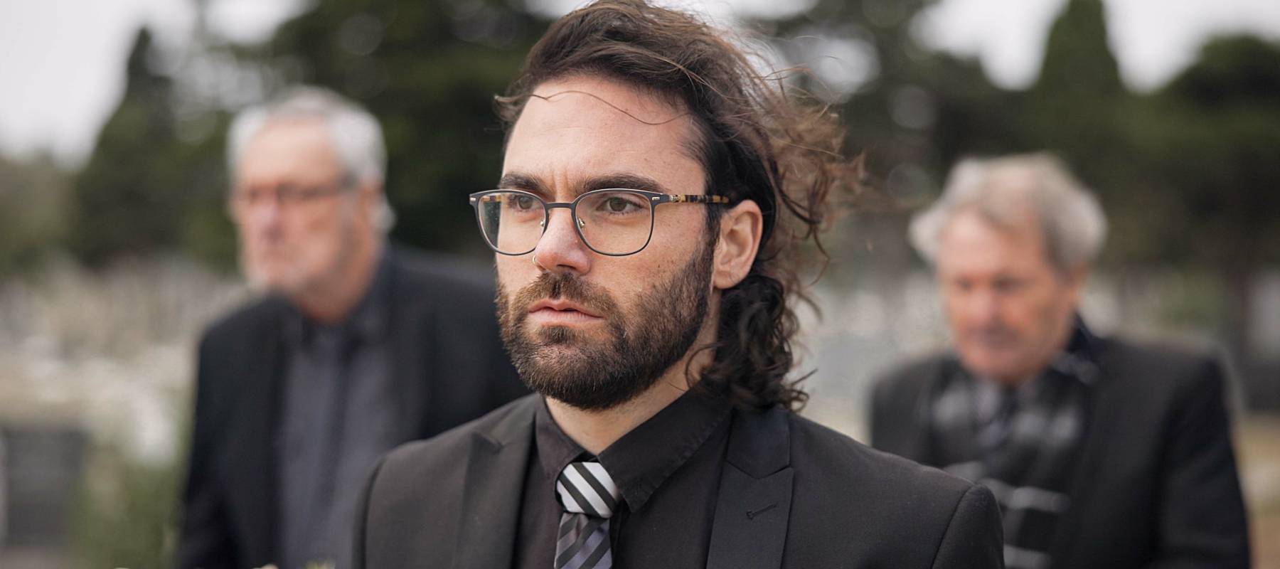 Caucasian man in his 30s, wearing glasses, attending a funeral service