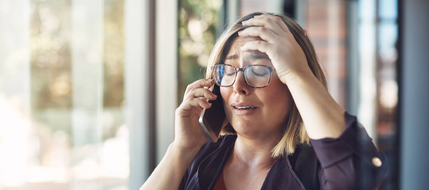 young Caucasian woman looking distraught while talking on a mobile phone in a modern office