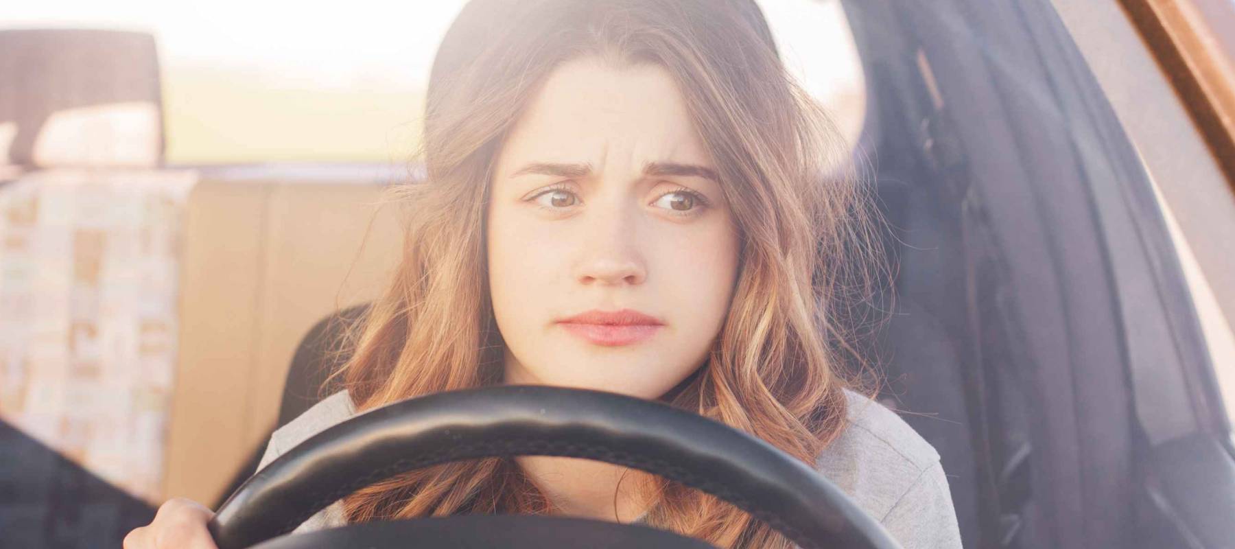 Nervous young woman, a first-time driver, sits at the wheel of a car