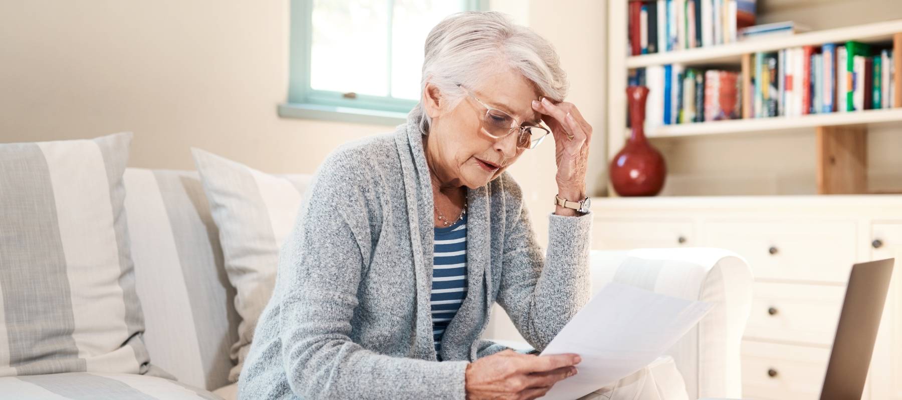 Older woman looking worried at bills while sitting on couch.