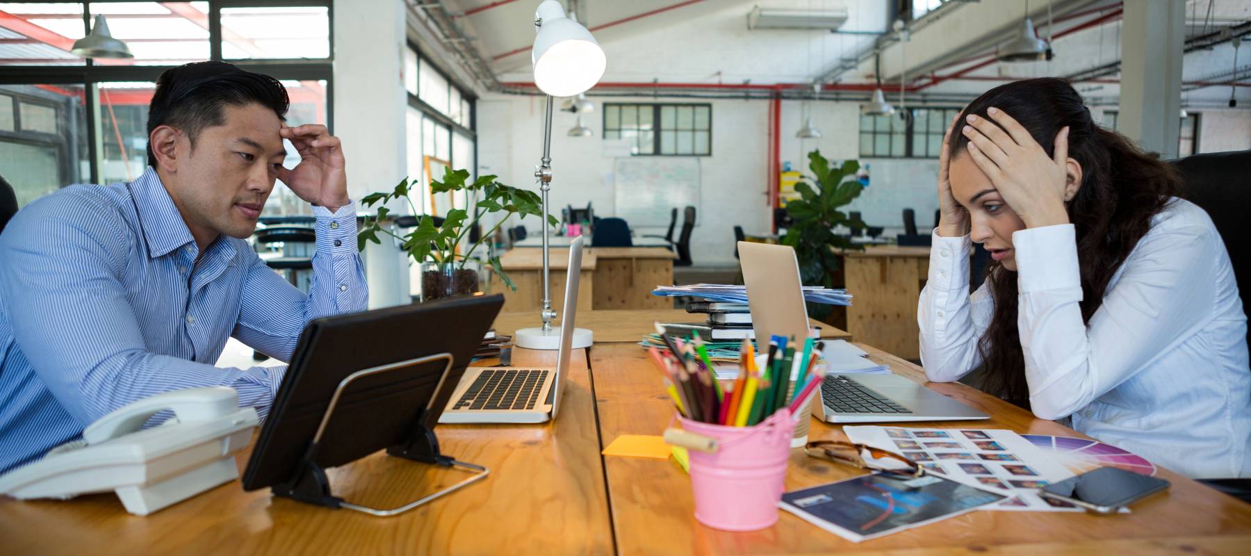 A pair of workers staring at their laptops, with worried expressions.