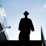 College graduate in silhouette wearing cap and gown and descending a stairway into a subway or underground garage