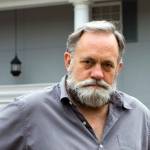 Unhappy homeowner poses in front of his two story columned southern home.