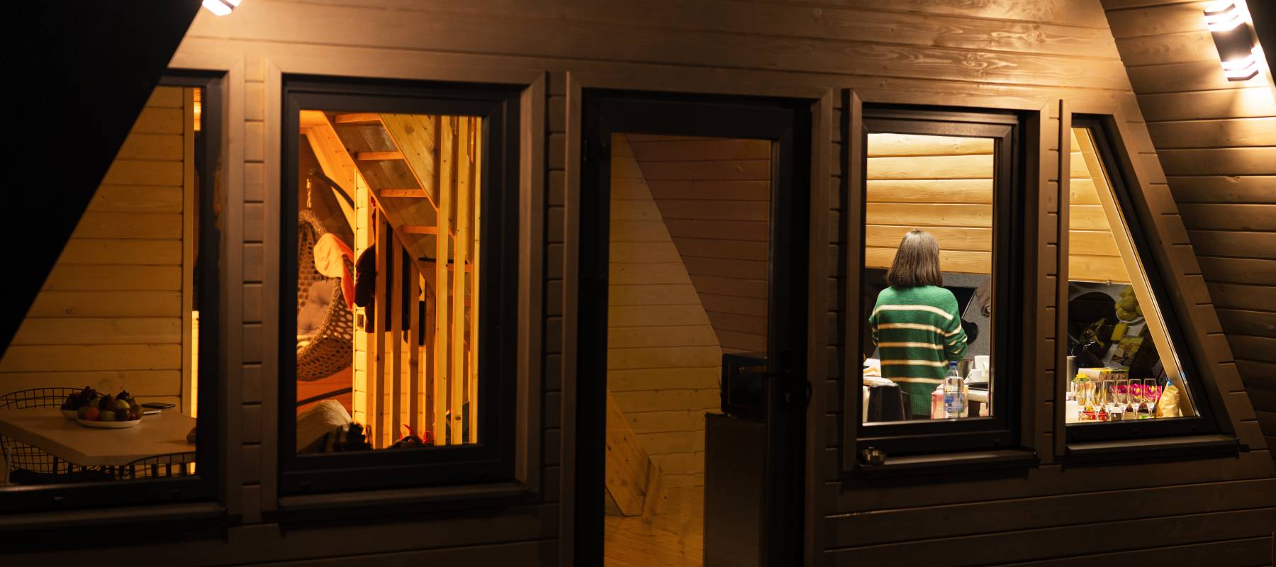 Woman prepares dinner in the kitchen. A view through the window of a country house at night.