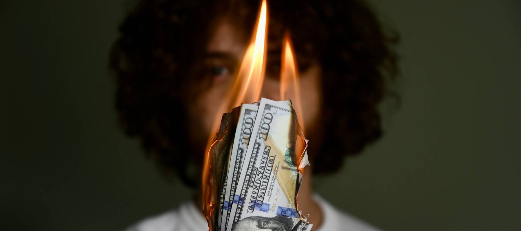 burning American money in the foreground, held up by a young Caucasian man