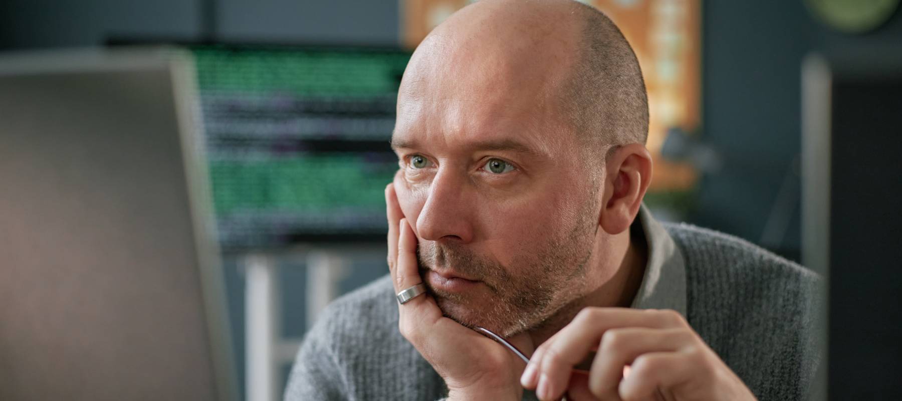 Middle-aged man resting his chin on his hand and looking worried, in front of laptop.