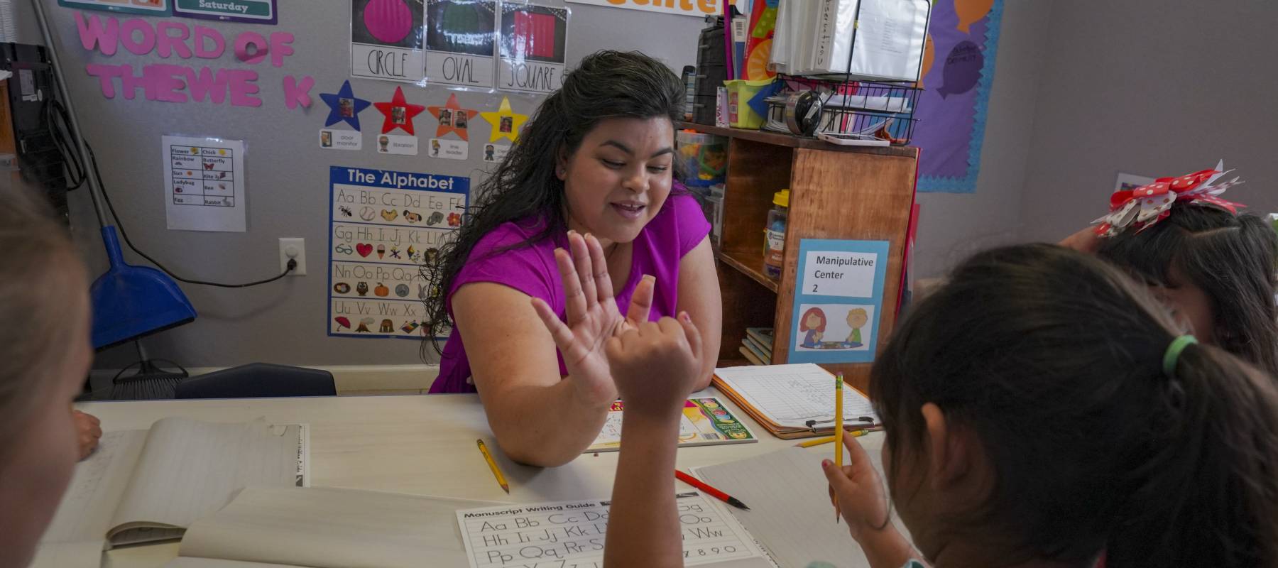 A teacher high-fiving a young student during writing practice at school.