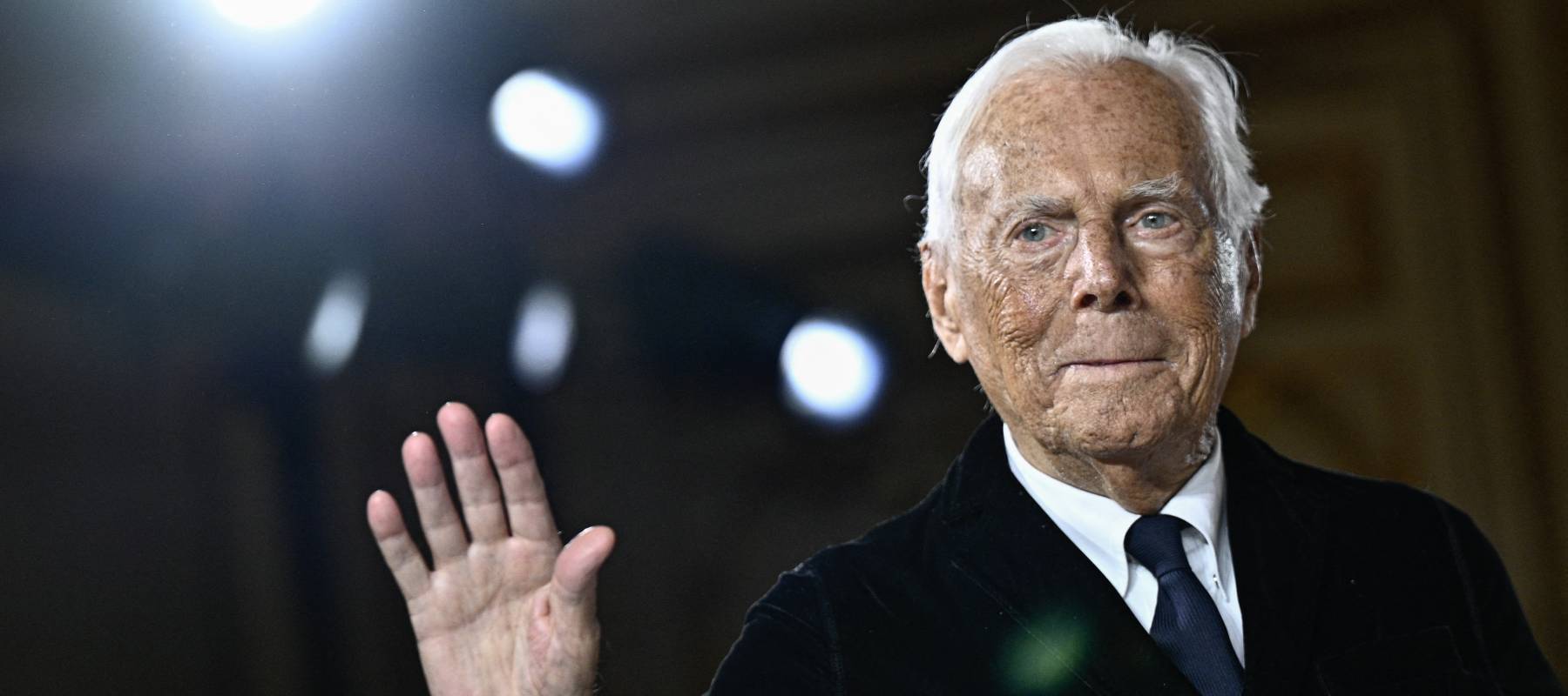 elderly Armani dressed in suit waves to audience