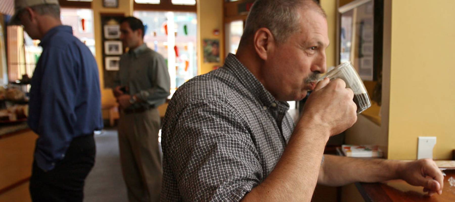 A man sipping a cup of coffee while sitting in a coffee shop.