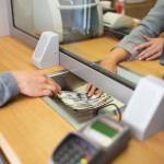 people, withdrawal, saving and finance concept - clerk giving cash money to customer at bank office or currency exchanger