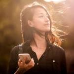 Young Asian-American woman holding cellphone in the sun