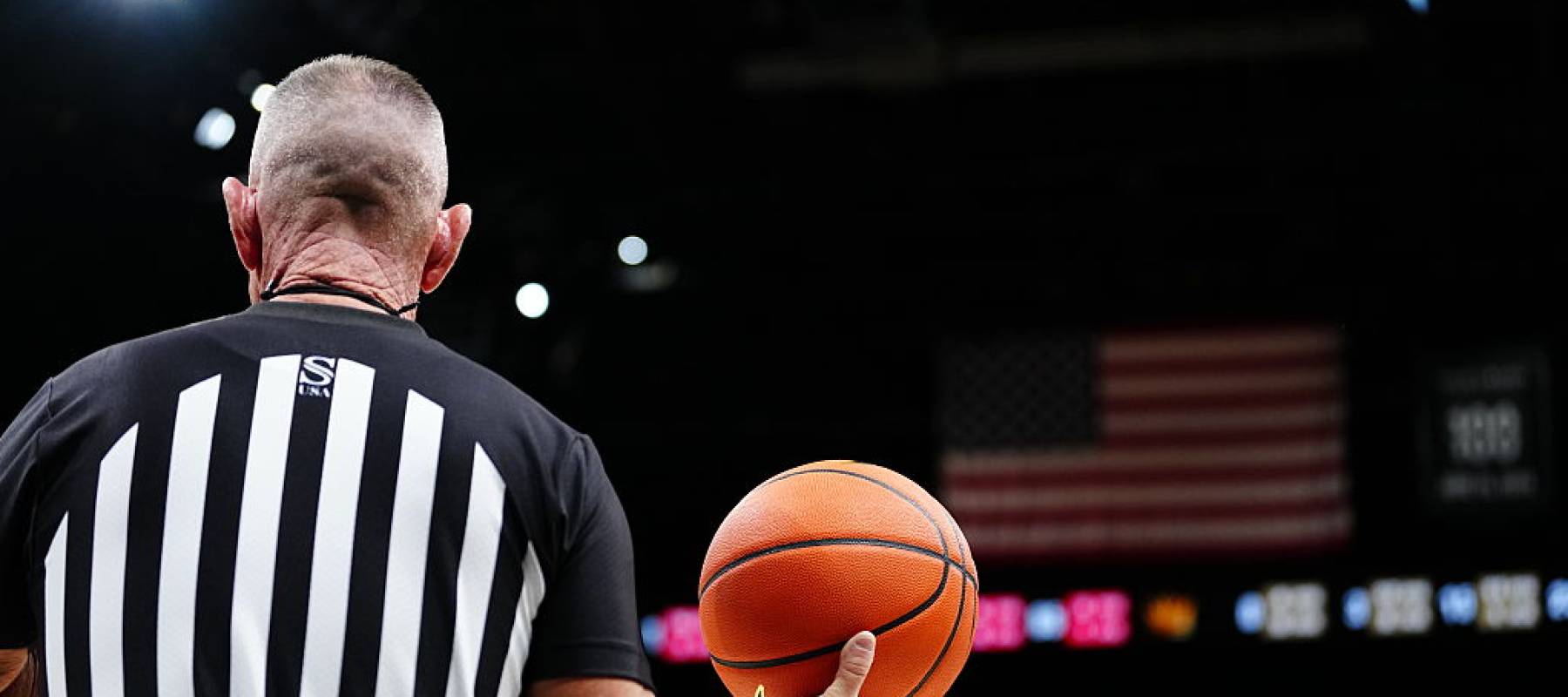 A referee holds a basketball in front of the US flag in the second half of a quarterfinal game of the College Basketball Crown tournament