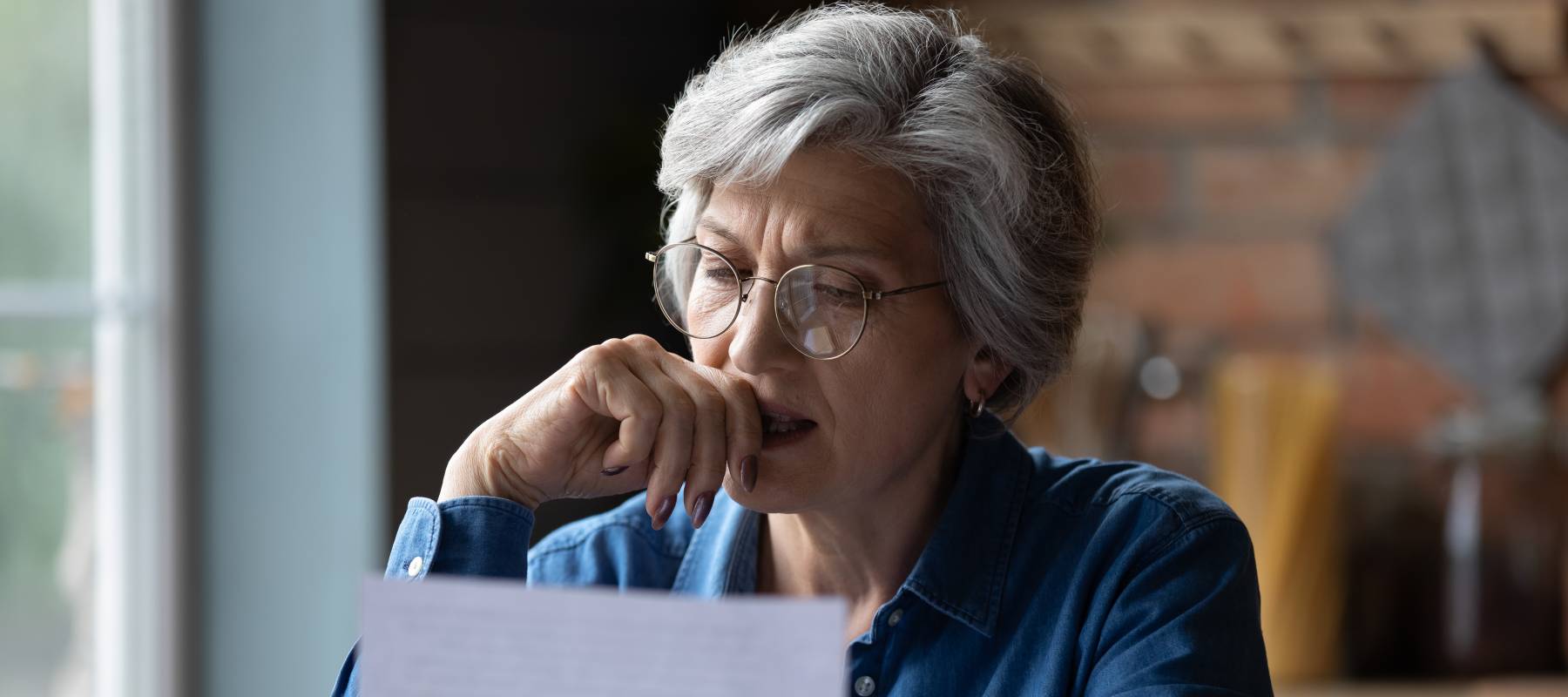 Older woman puts her hand to her face while looking at a piece of paper, concerned.
