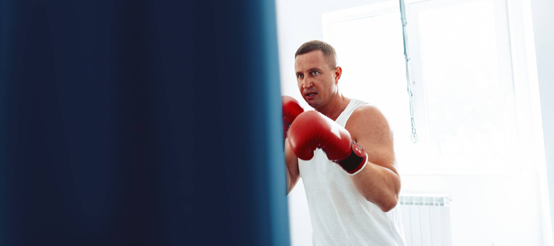 middle-aged boxer training in a gym, fighting with punching bag close up