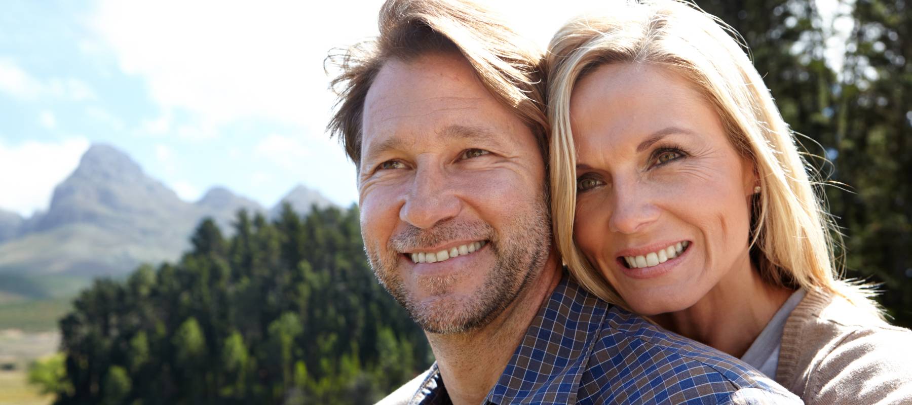 Smiling middle-aged couple standing on a dock at a lake.