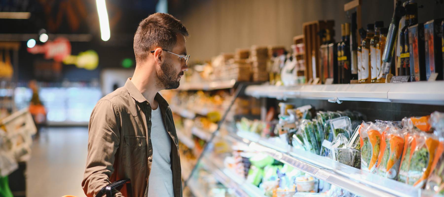 A man carefully surveys his food options at a grocery store.