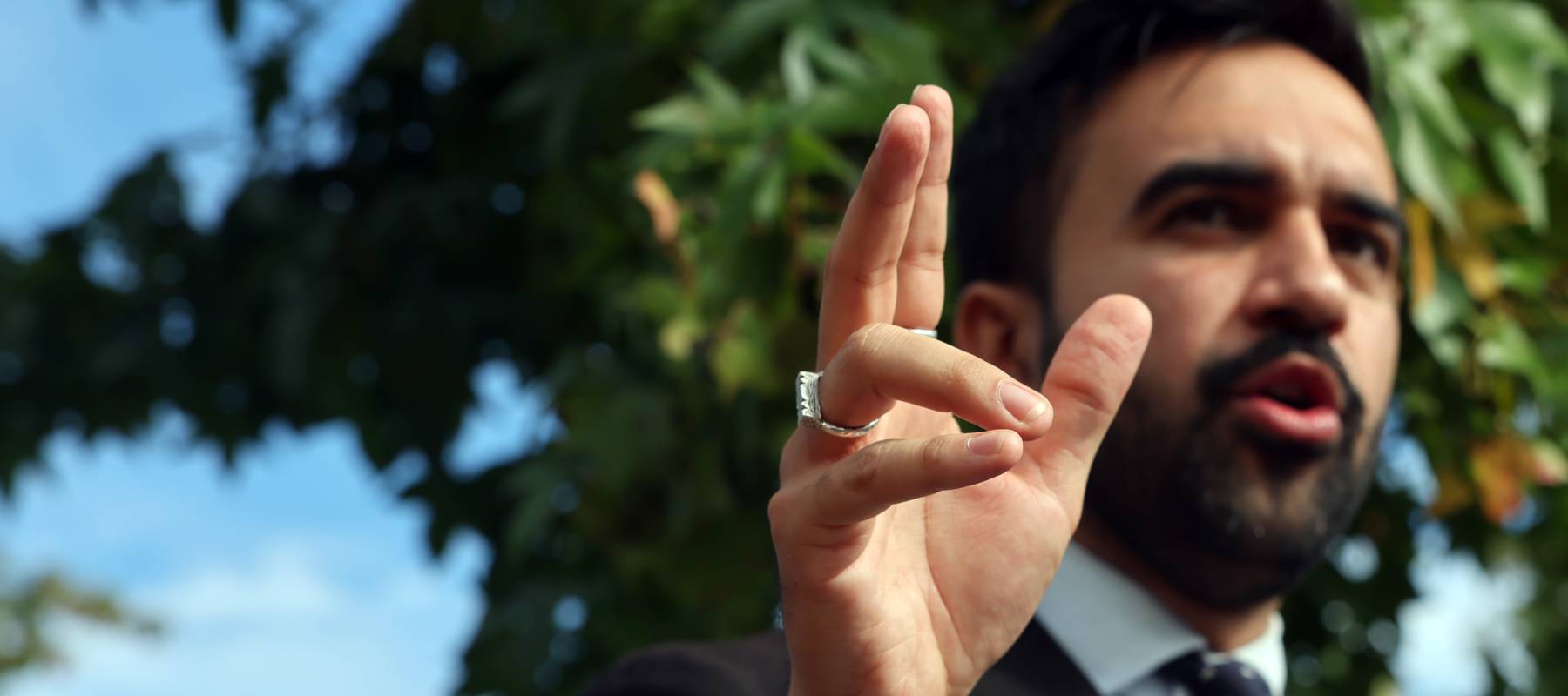 Zohran Mamdani smiles at a tenant bloc event outdoors with red signs