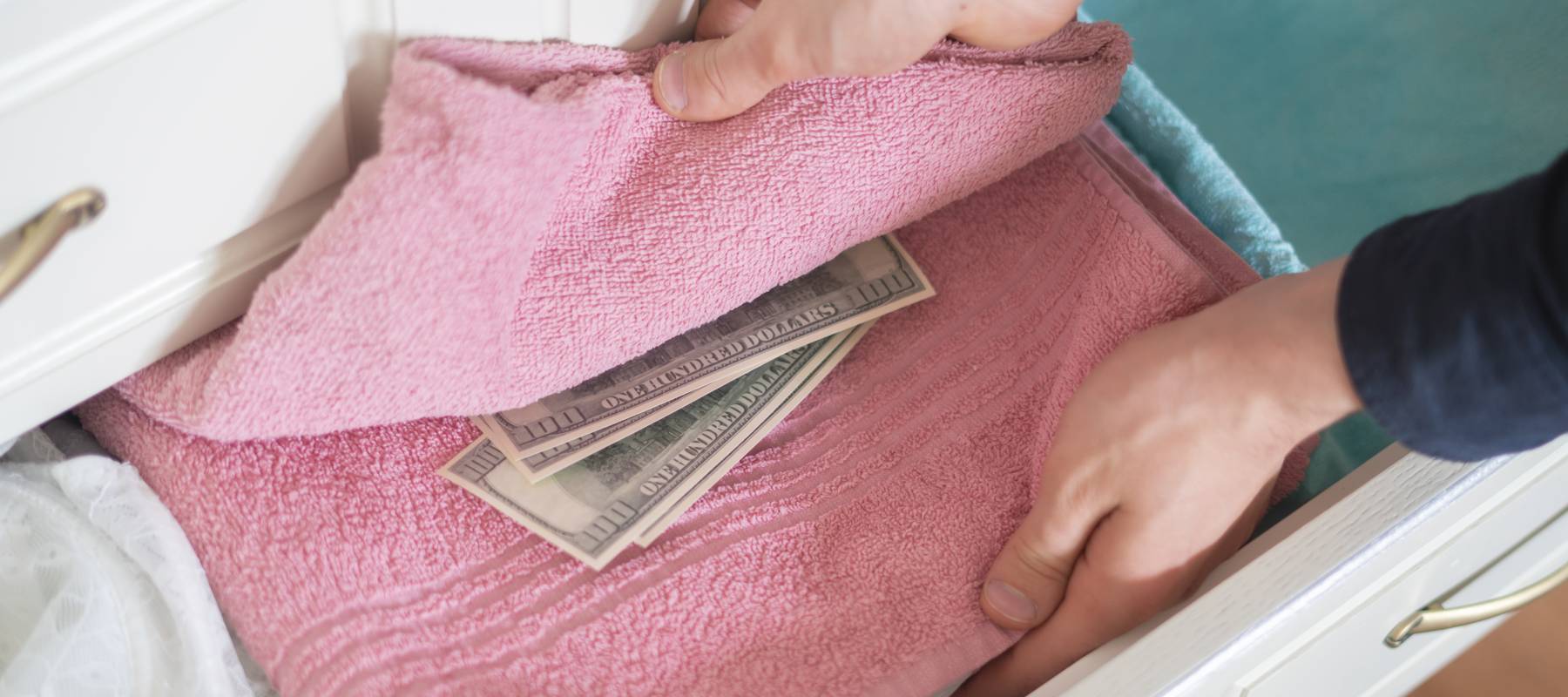 hand taking hidden stash of cash money from the wardrobe at home
