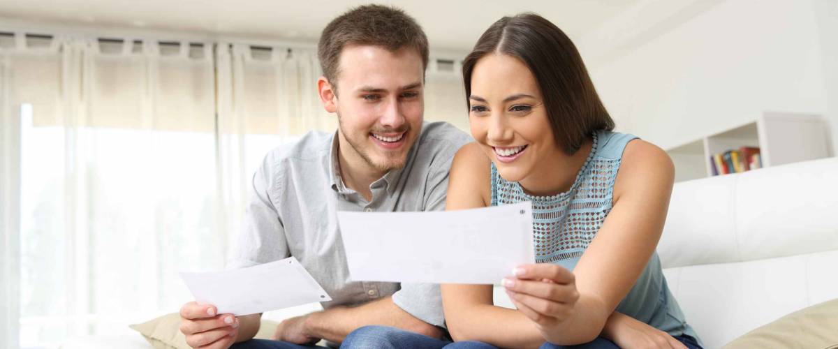 Happy young couple looking and checking bills on a couch at home