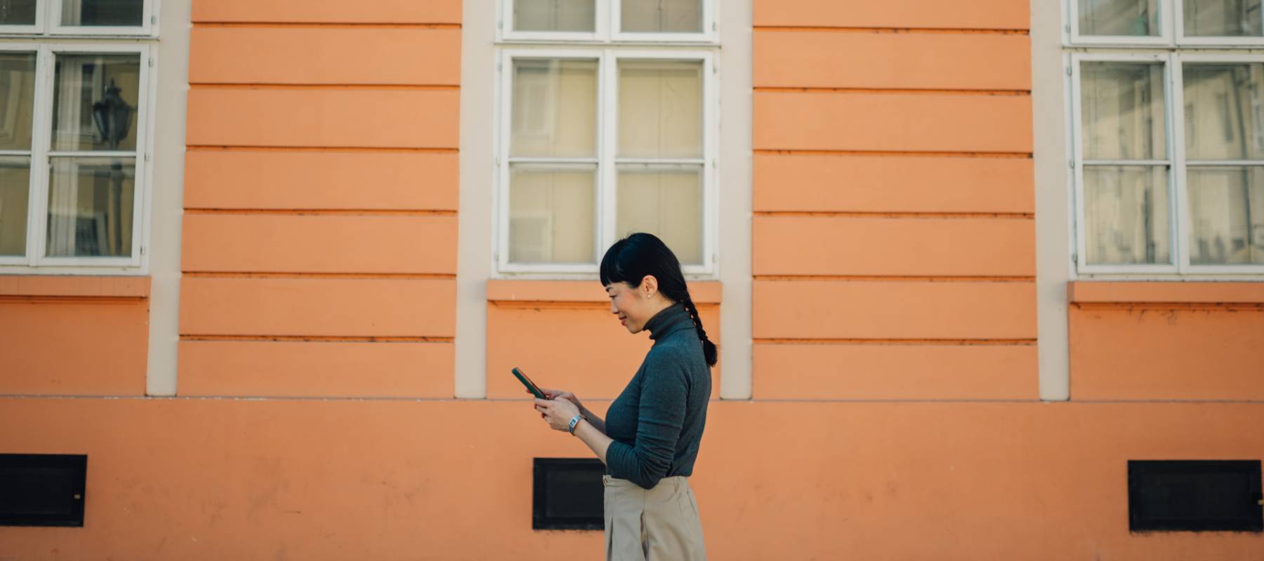 woman looks at tablet in front of pretty orange house