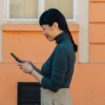 woman looks at tablet in front of pretty orange house