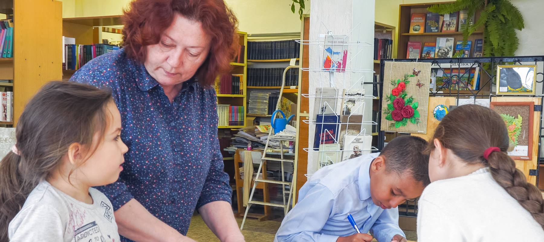 Older woman works in school classroom with elementary students doing a craft